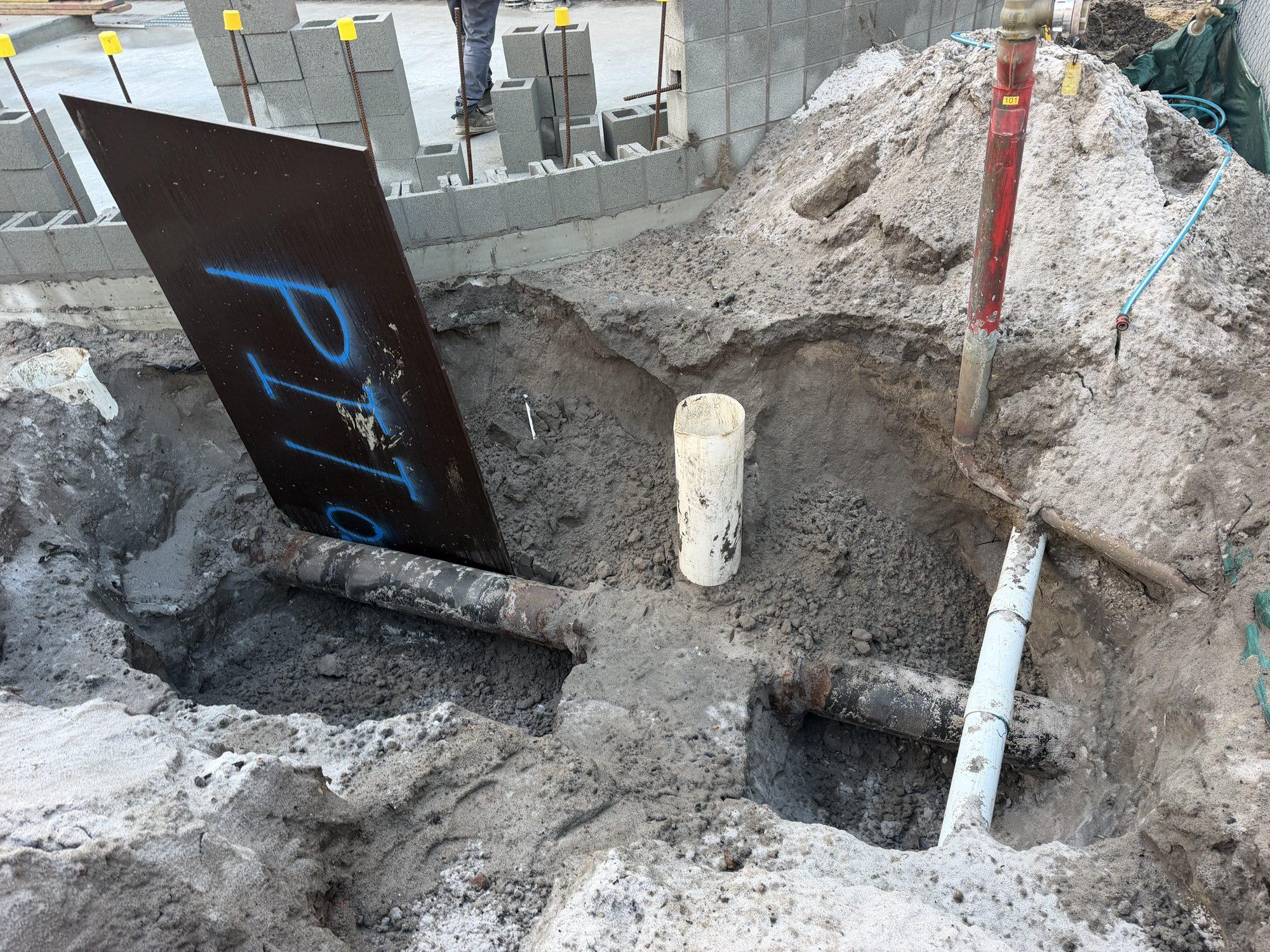 The old water main exposed in the excavation with pit boards over the openings