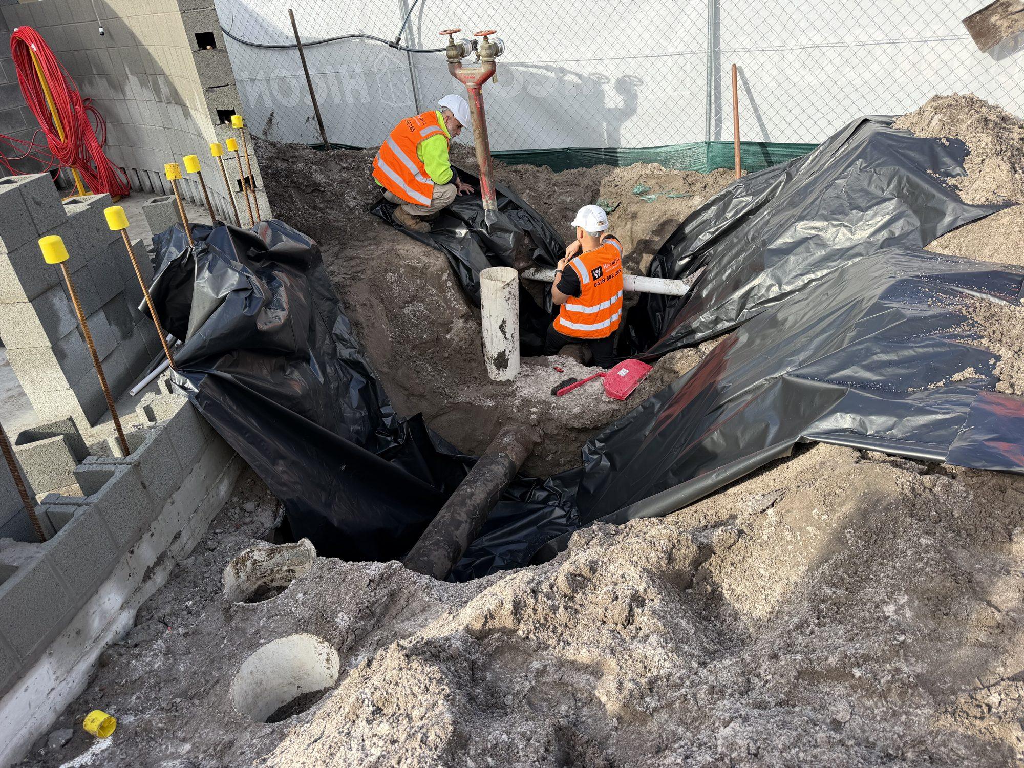 HazWreck crew working in the plastic-lined excavation around the asbestos-coated pipe