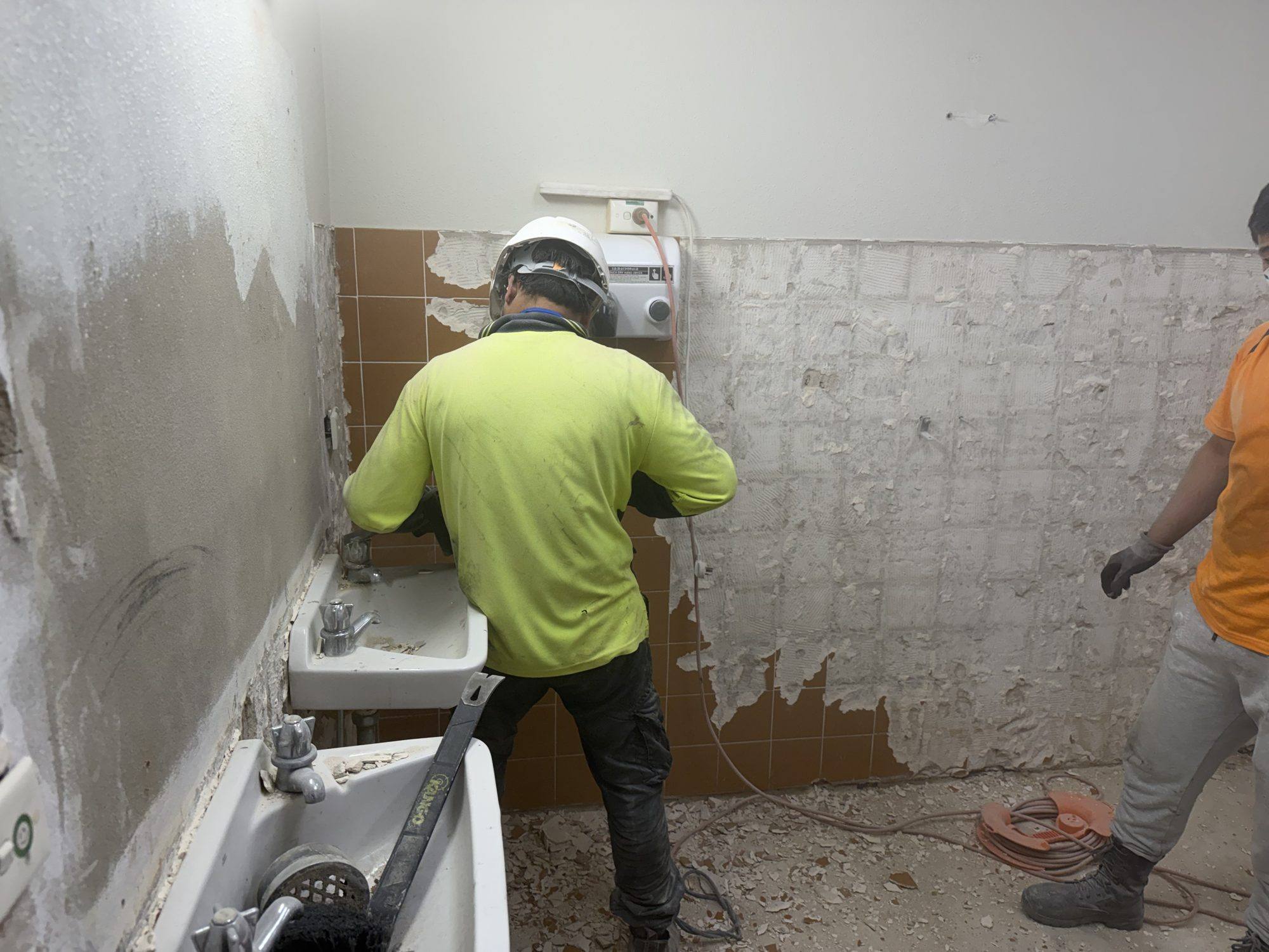 HazWreck crew member grinding tiled walls back to substrate in a bathroom strip-out