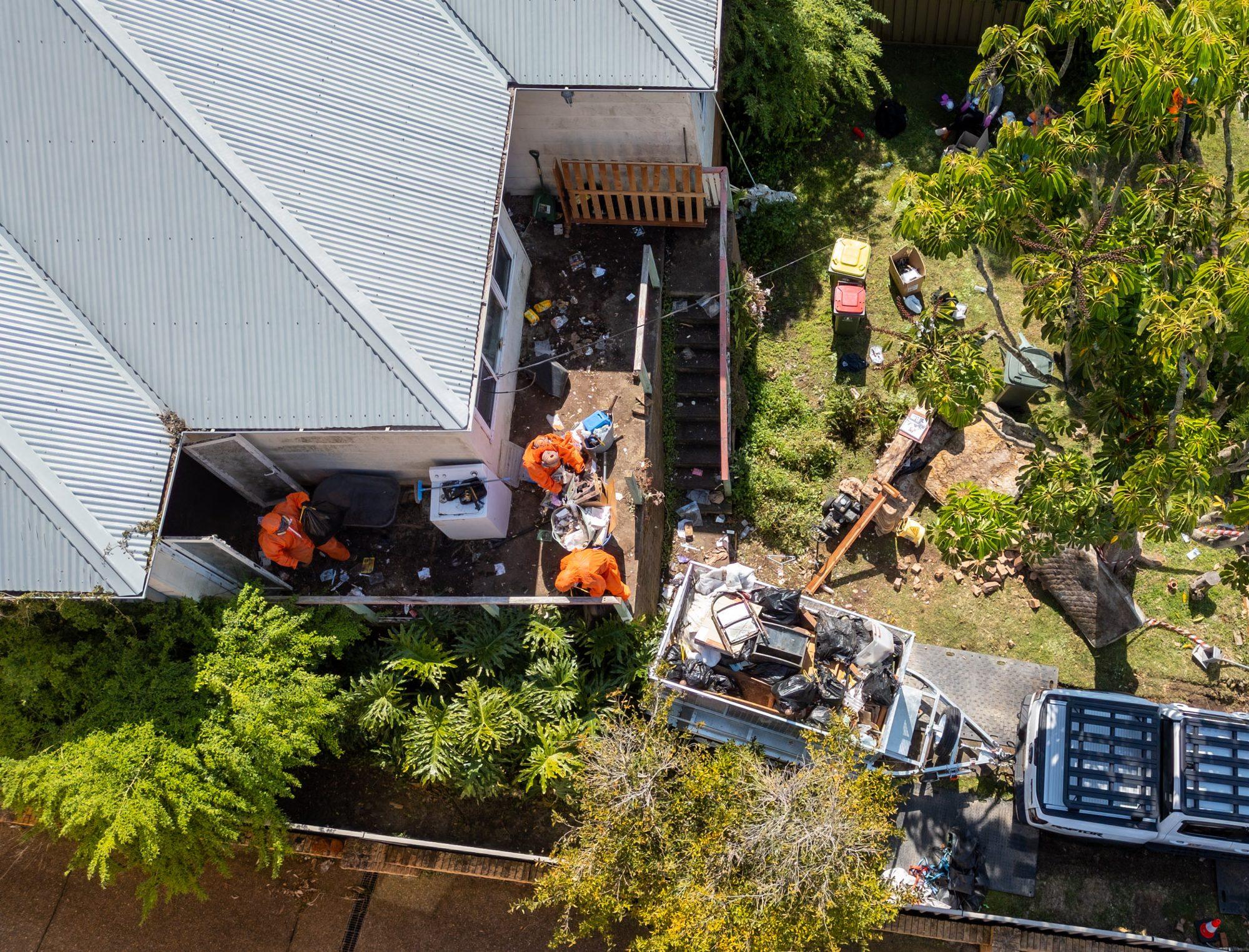 Drone view of a HazWreck house clean-out in Sydney — crew in PPE at the back door, cage trailer filling in the driveway