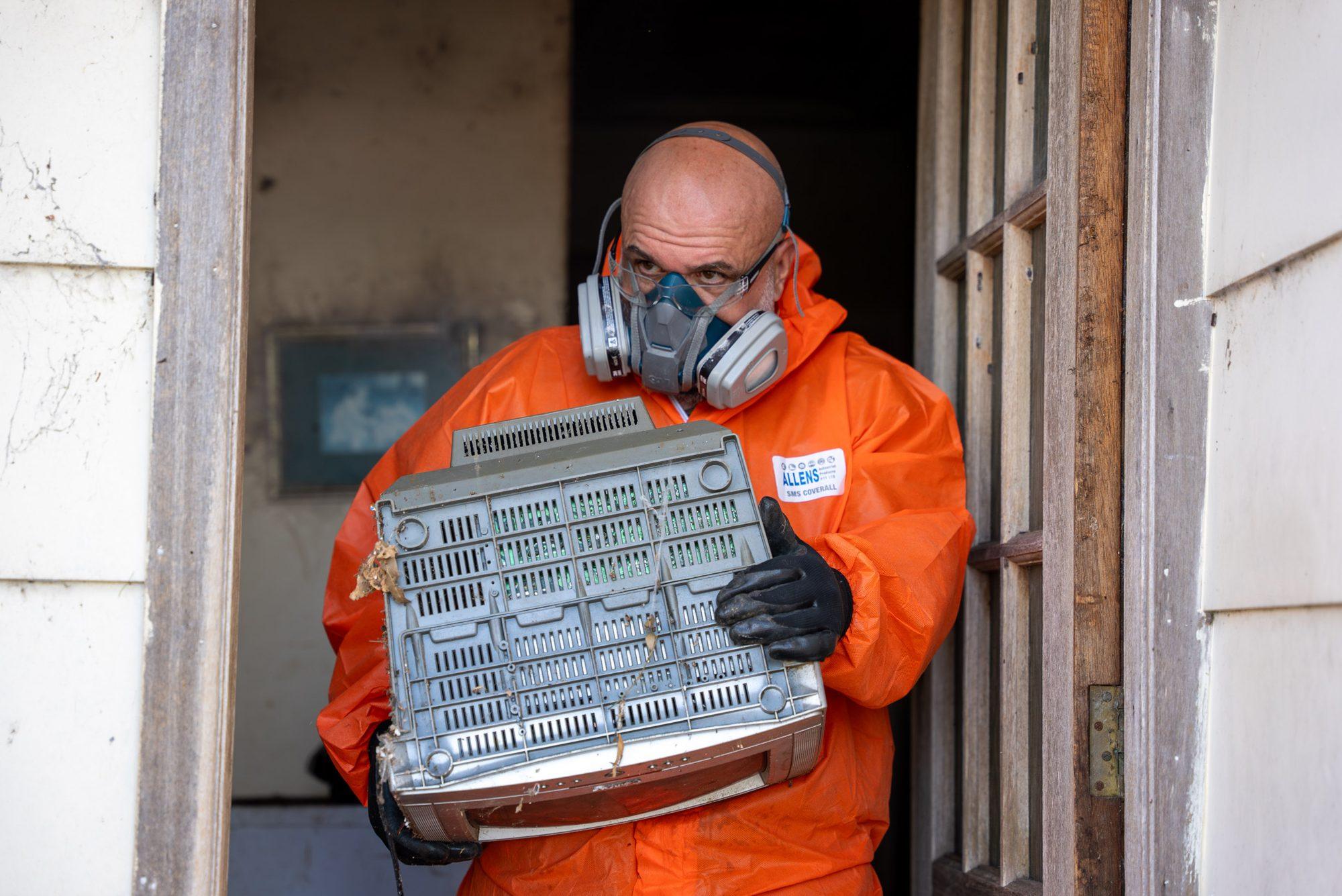 HazWreck crew member in PPE carrying an old appliance out through the front door of a Sydney home