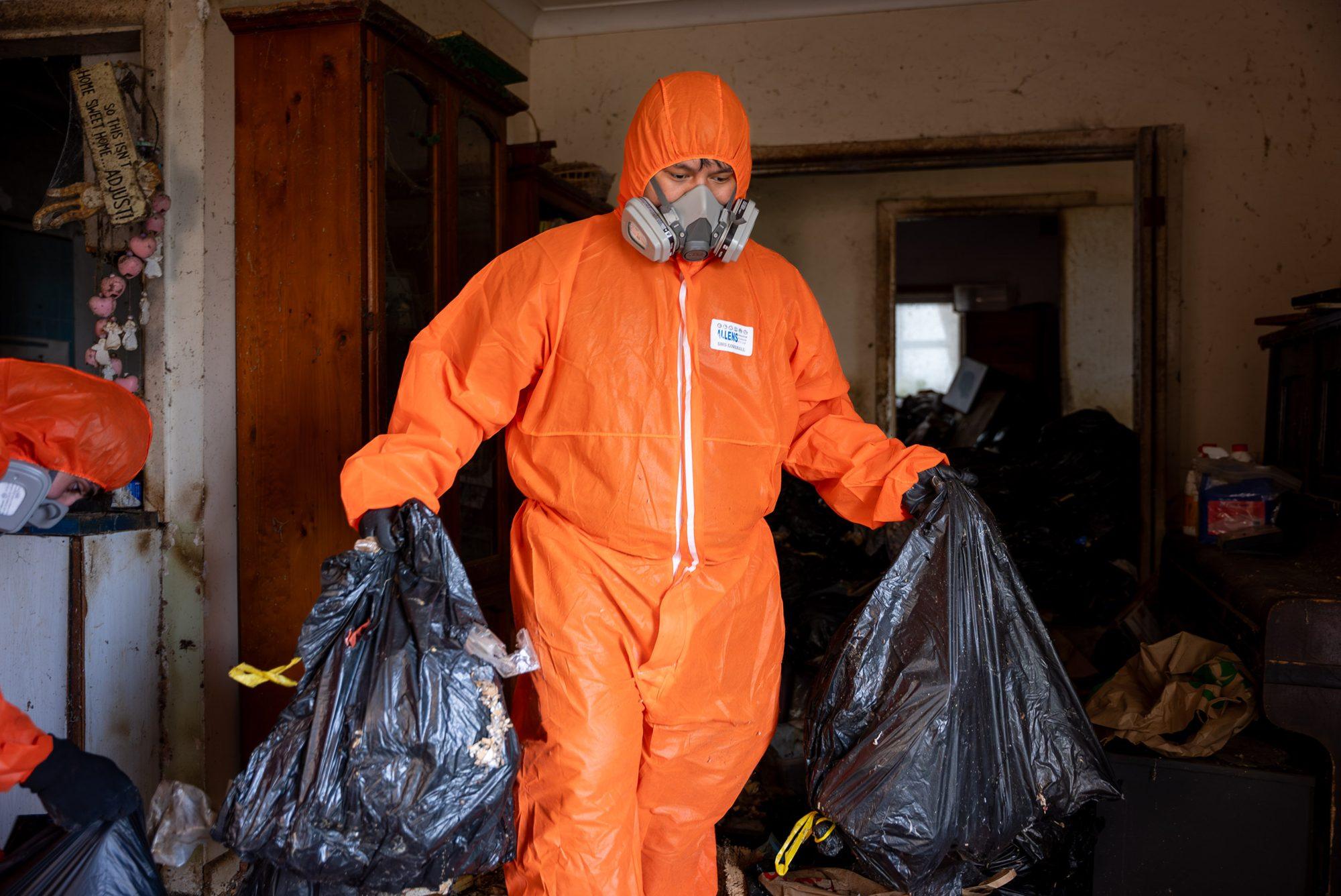 HazWreck crew member in PPE carrying bagged contents through a Sydney lounge room