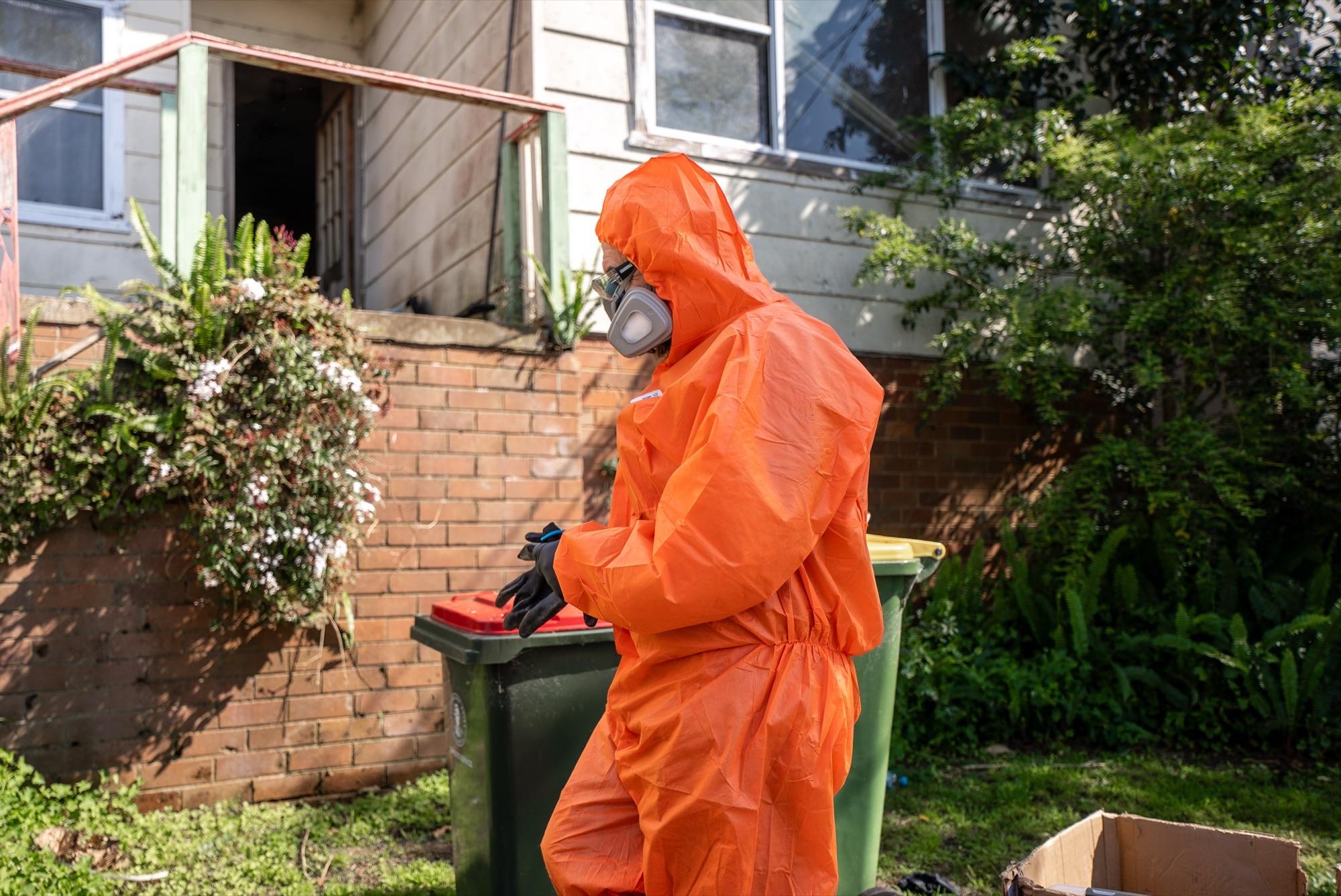 Crew member in PPE carrying material out to the bins at a weatherboard house