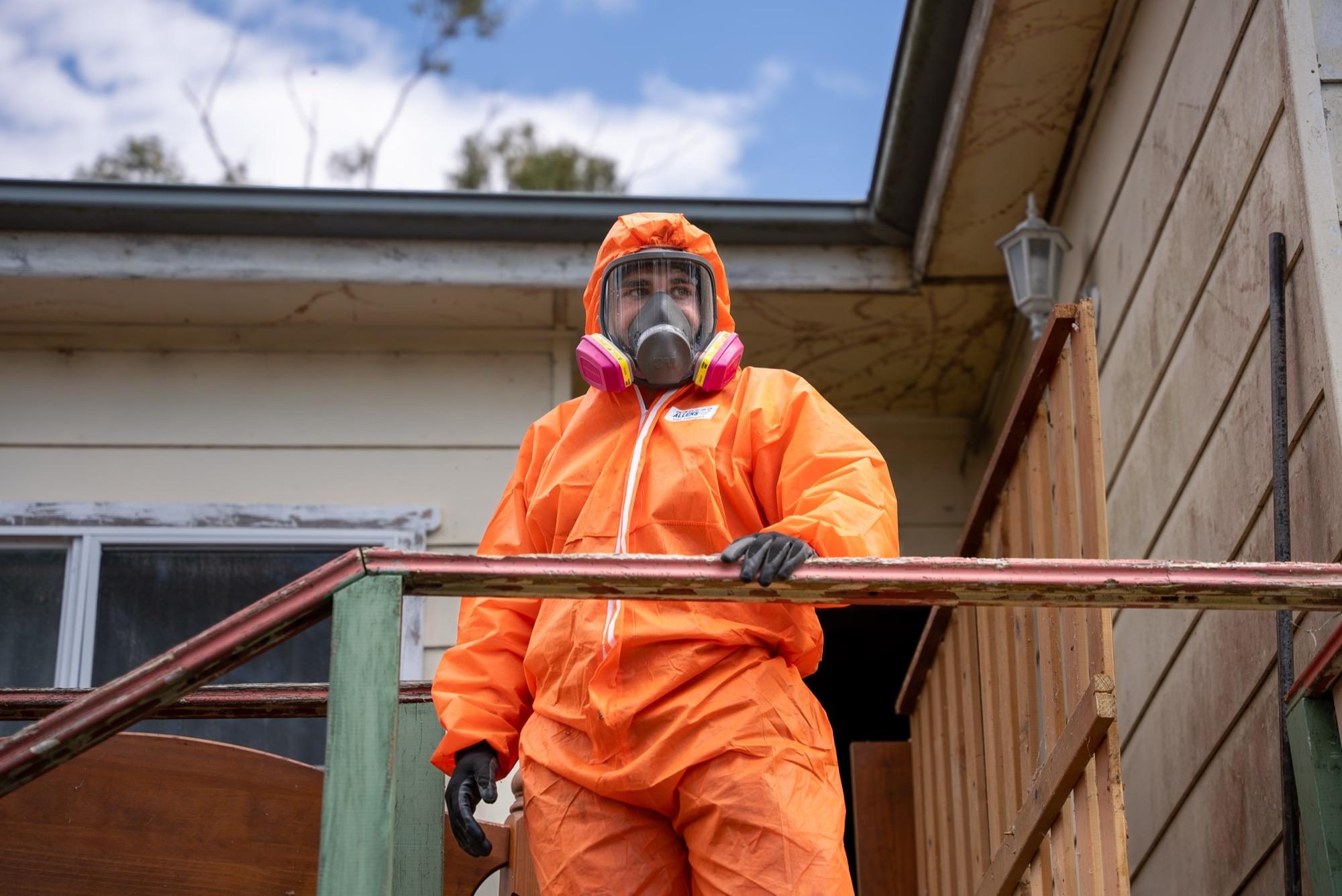 HazWreck crew member in full-face respirator and coveralls on the verandah of a Sydney weatherboard home