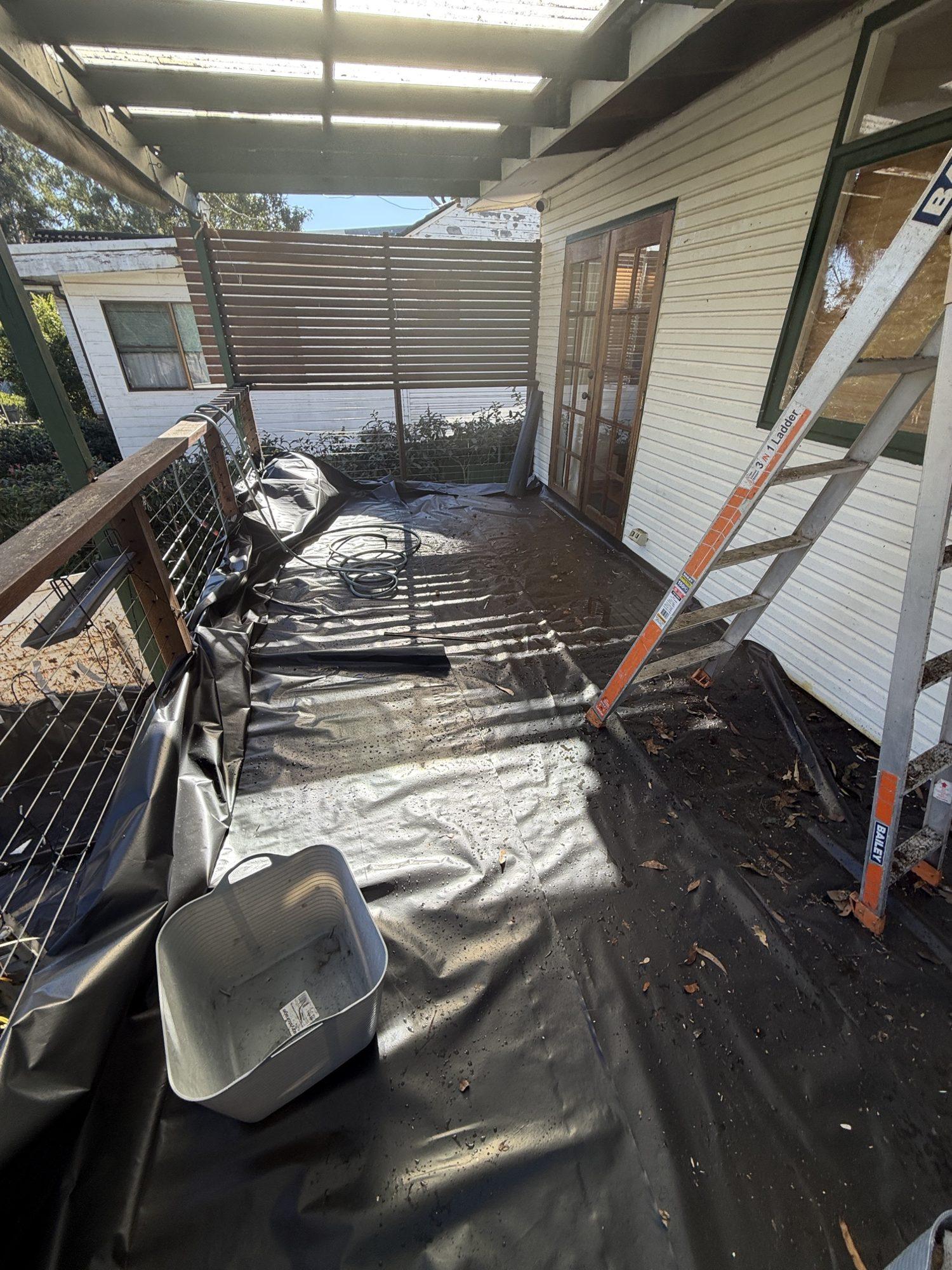 Heavy plastic sheeting laid over a timber deck beneath the eaves, with a ladder, before removal