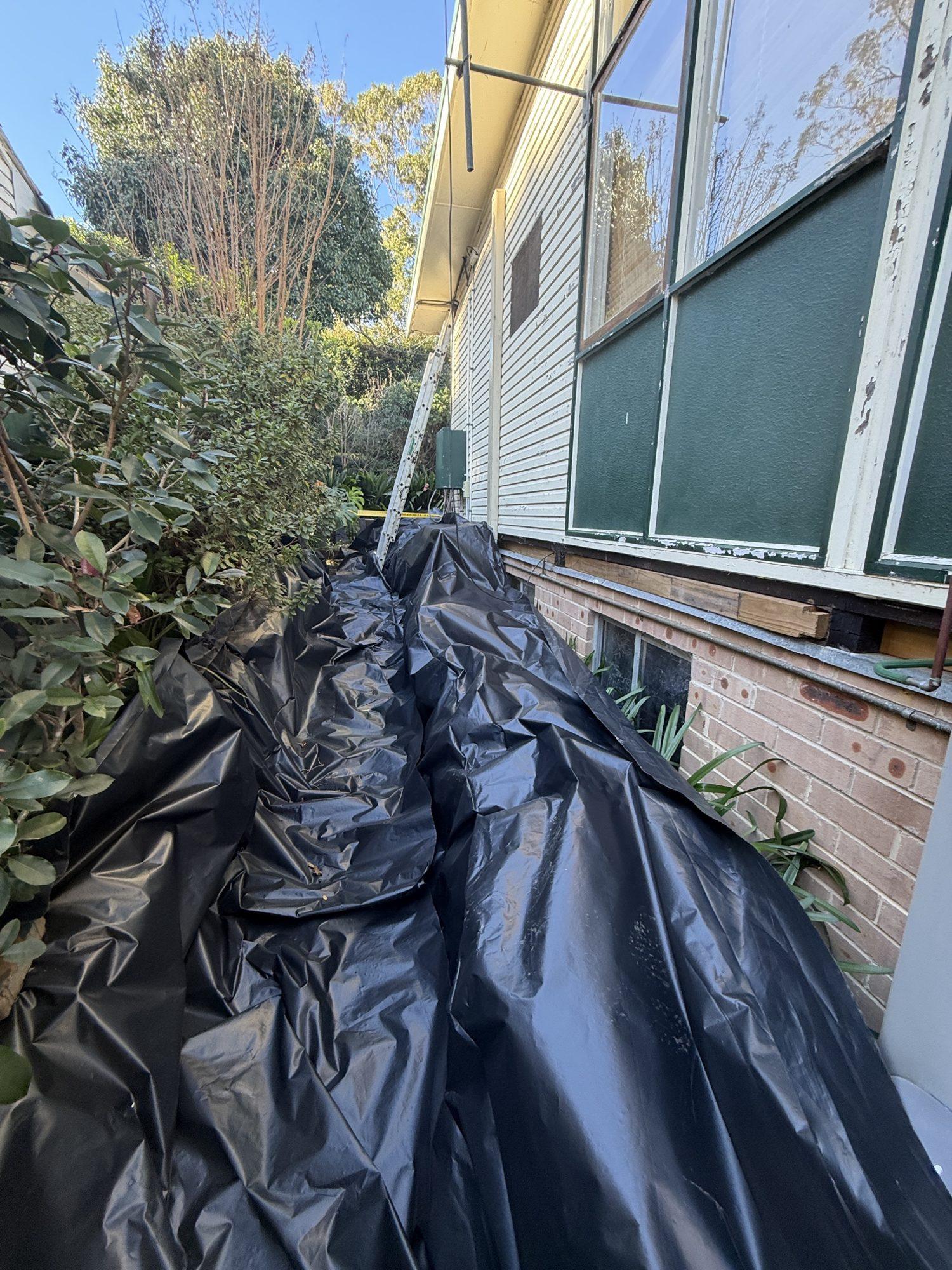 Removed asbestos sheets wrapped in black plastic along the side passage of the house