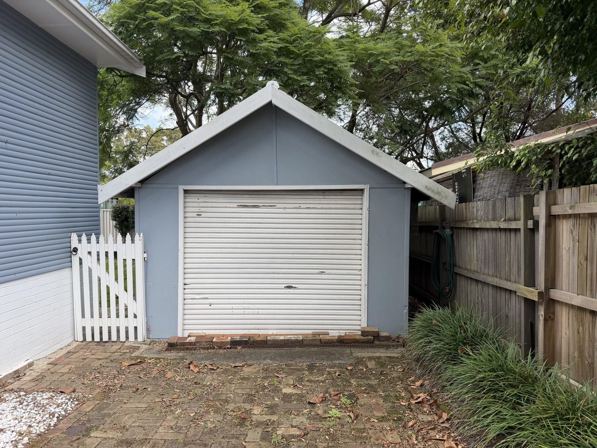 Front of the blue fibro garage with its white roller door before demolition