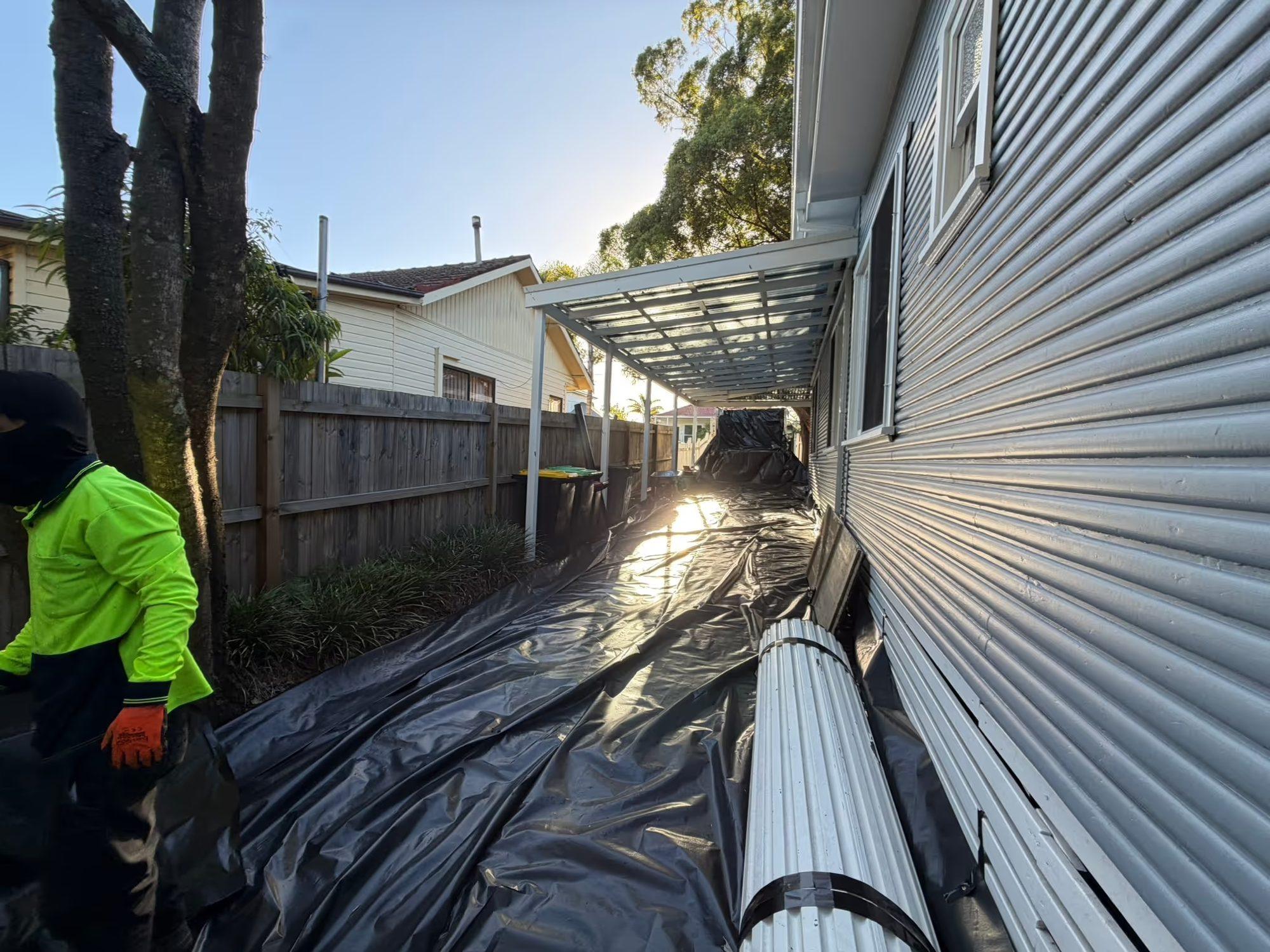 Crew member carrying Super Six roof sheets down the plastic-sheeted side path