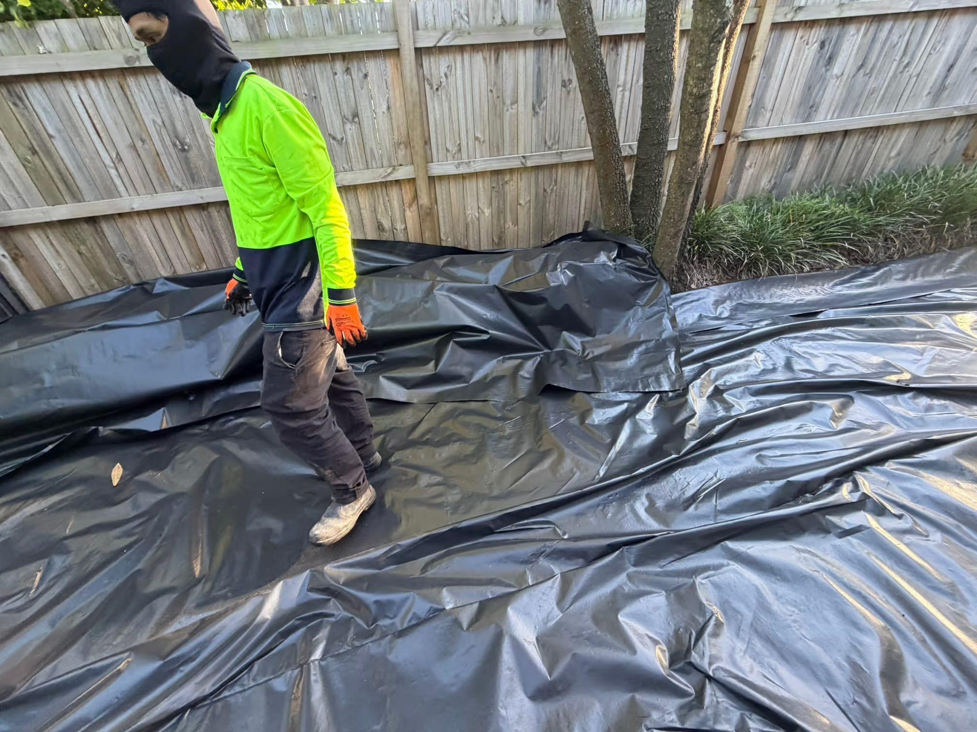 Removed asbestos sheeting laid out on heavy black plastic for double-wrapping