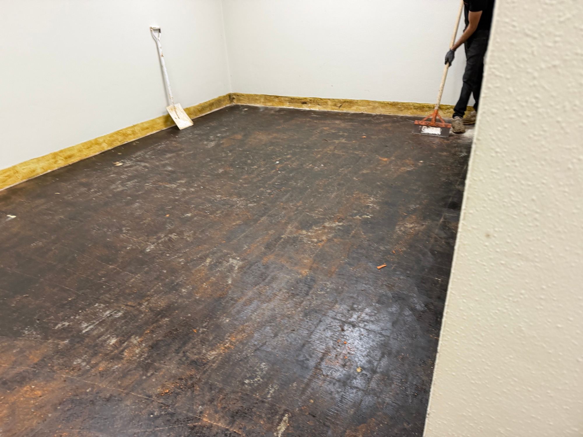 Gym floor covered in black vinyl adhesive after the coverings were lifted, before grinding