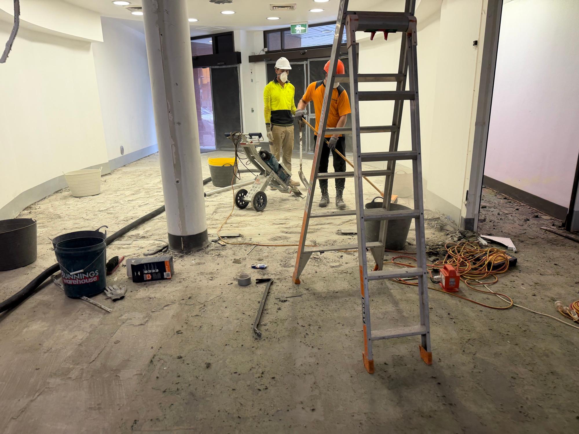 HazWreck crew in masks and hi-vis grinding the floor of a stripped Gladesville gym tenancy