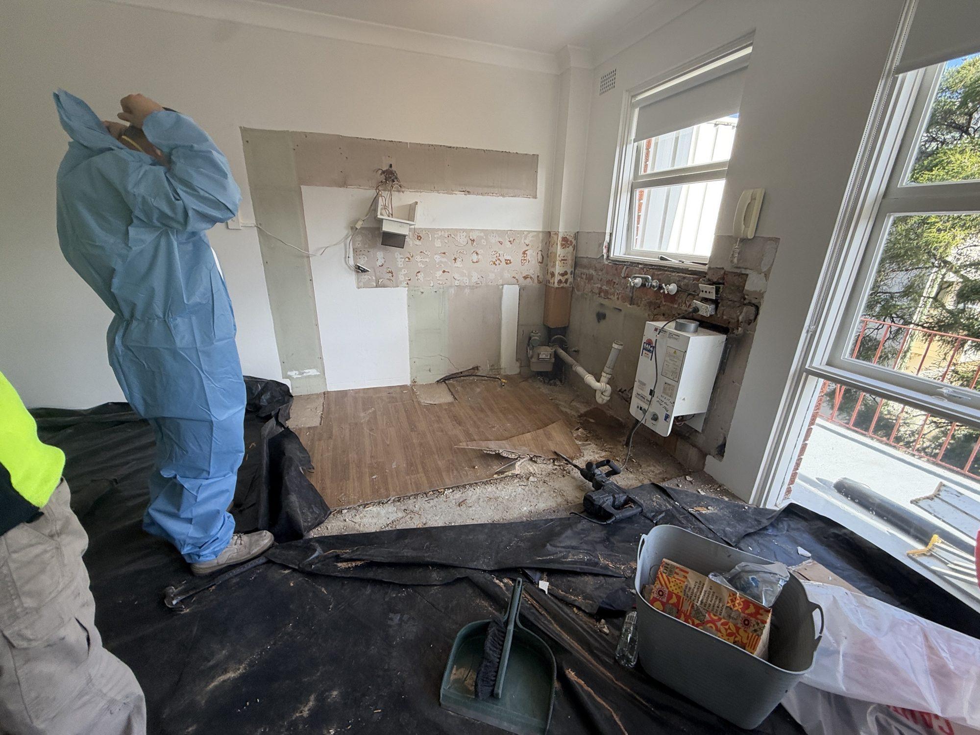 HazWreck removalist in disposable coveralls lifting the asbestos vinyl floor in the stripped kitchen