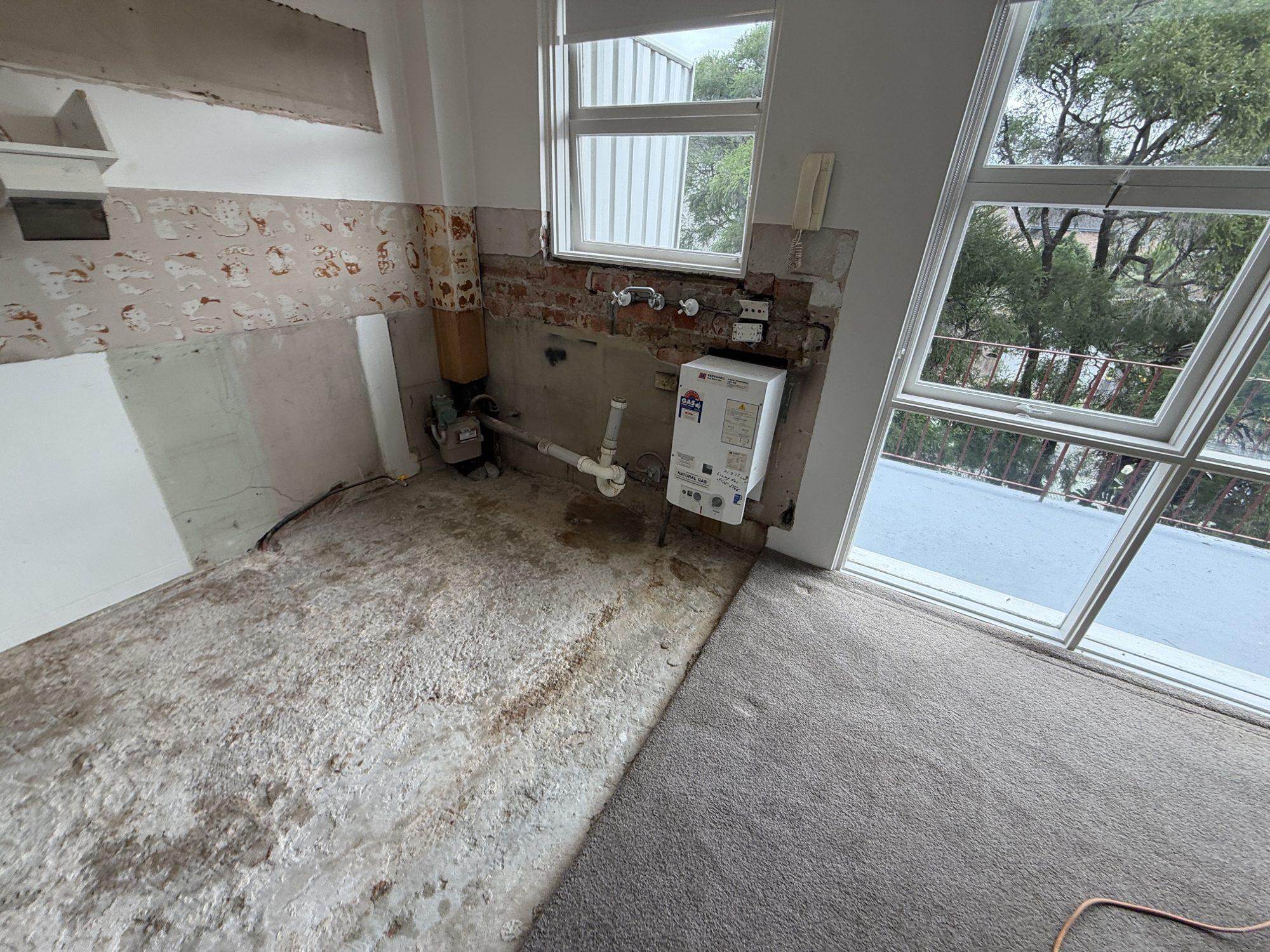 Kitchen stripped to bare brick and slab with plumbing stubs exposed after the asbestos floor removal