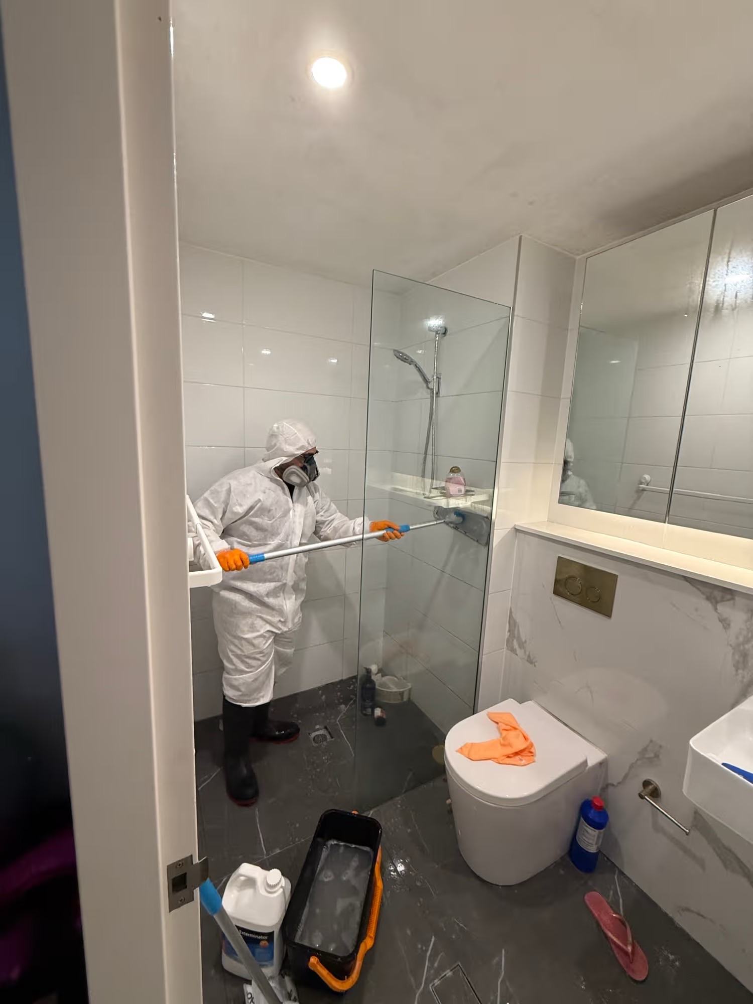 HazWreck crew member in white PPE and respirator treating the bathroom ceiling with a pole
