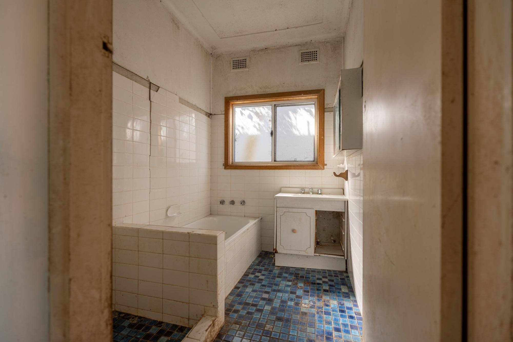 Original 1960s Sydney bathroom with stained walls — where mould and fibro sheeting usually meet