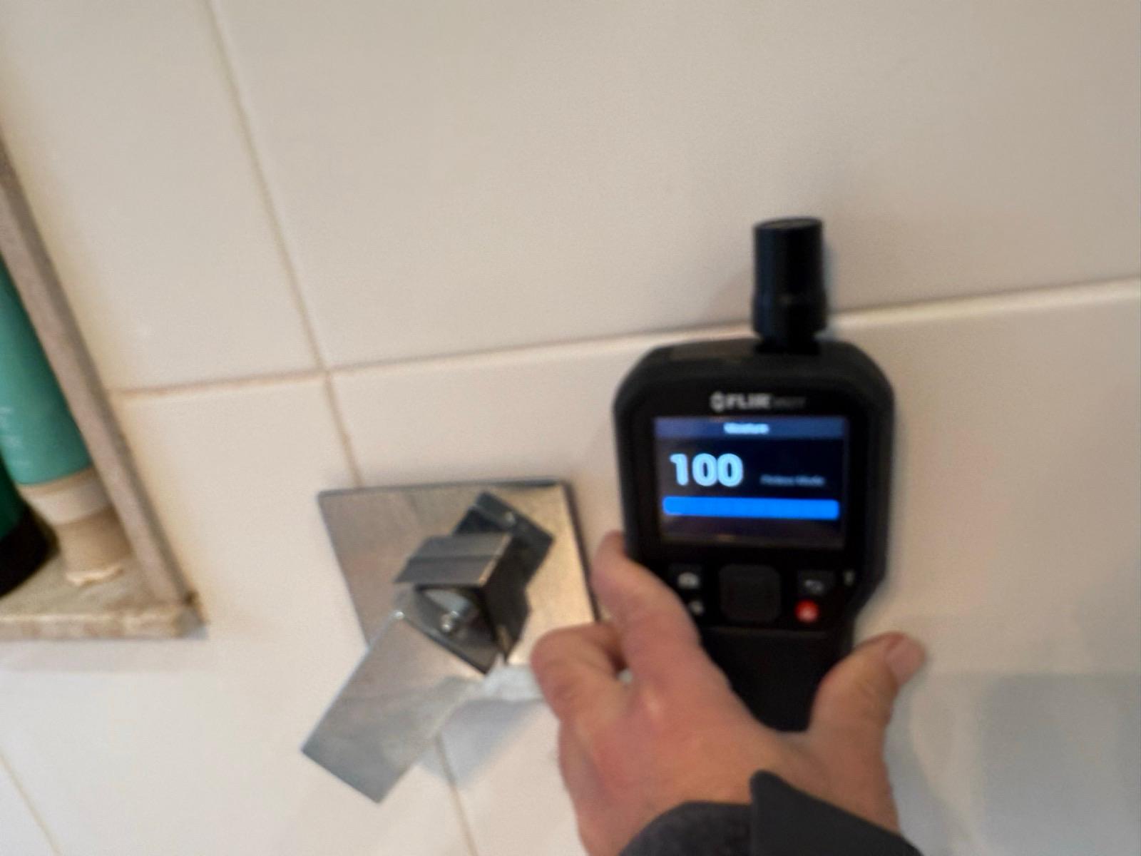 Moisture meter reading 100 on a tiled bathroom wall
