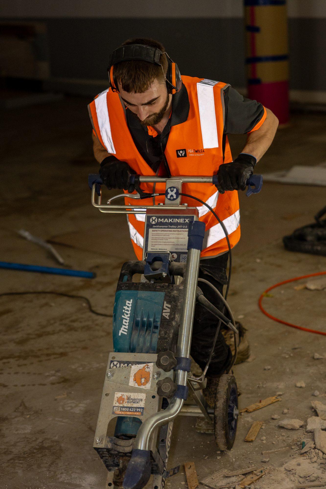 HazWreck worker running a trolley-mounted breaker across the floor at the Plus Fitness Manly Vale site