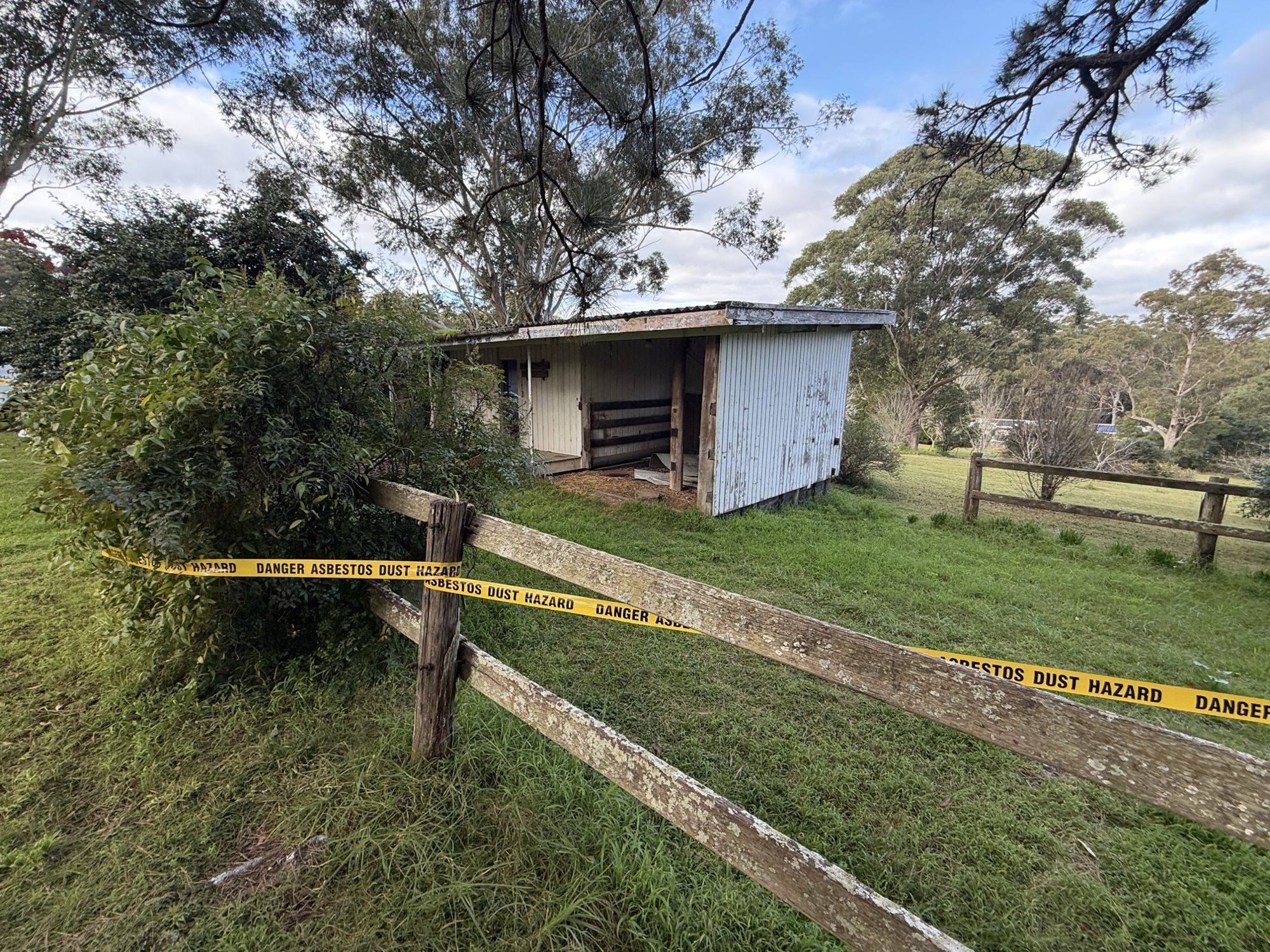 Asbestos exclusion-zone tape across the fence line before demolition works at Dural