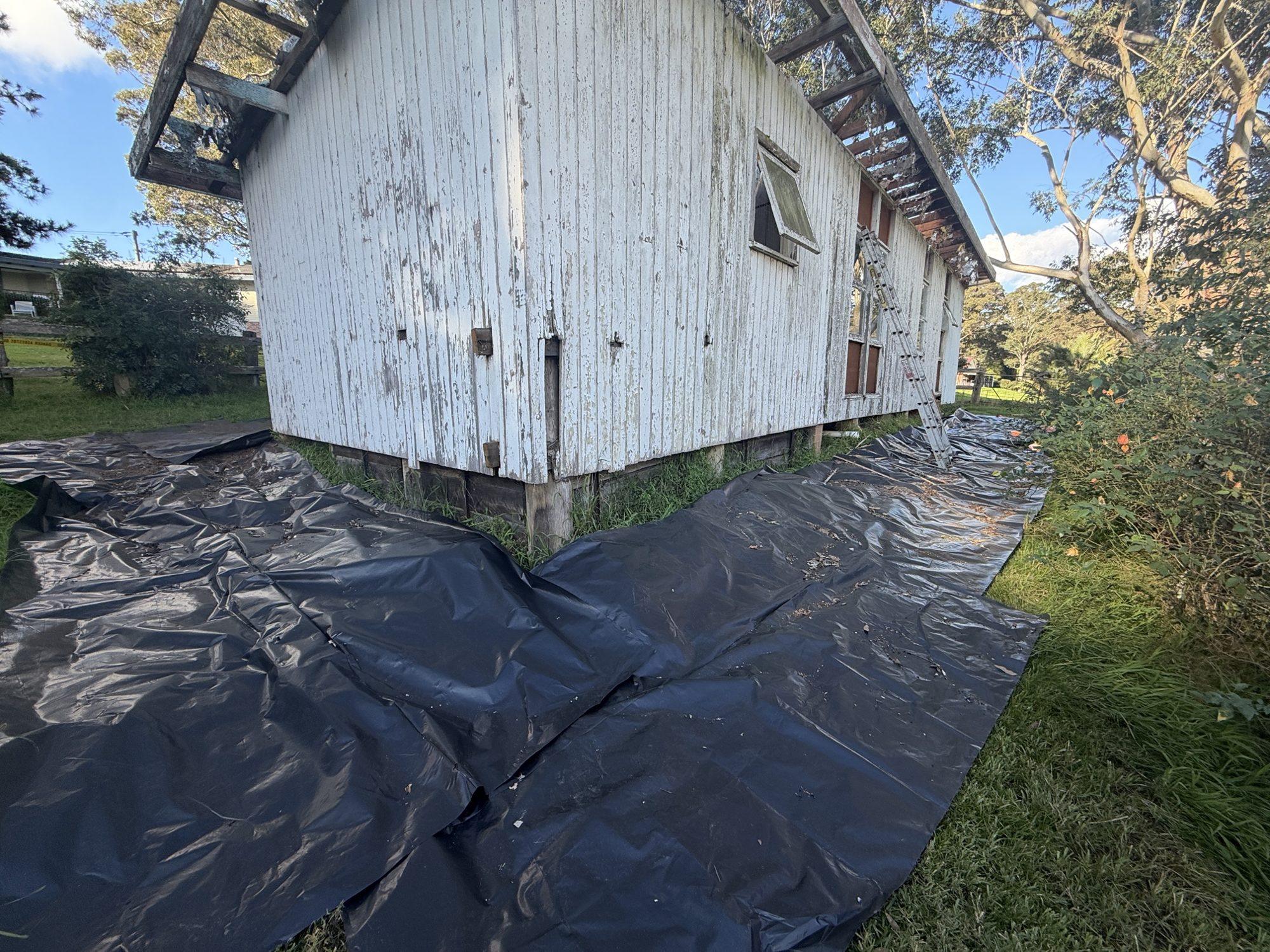 Shed with its roof removed and black plastic containment sheeting laid on the ground around it
