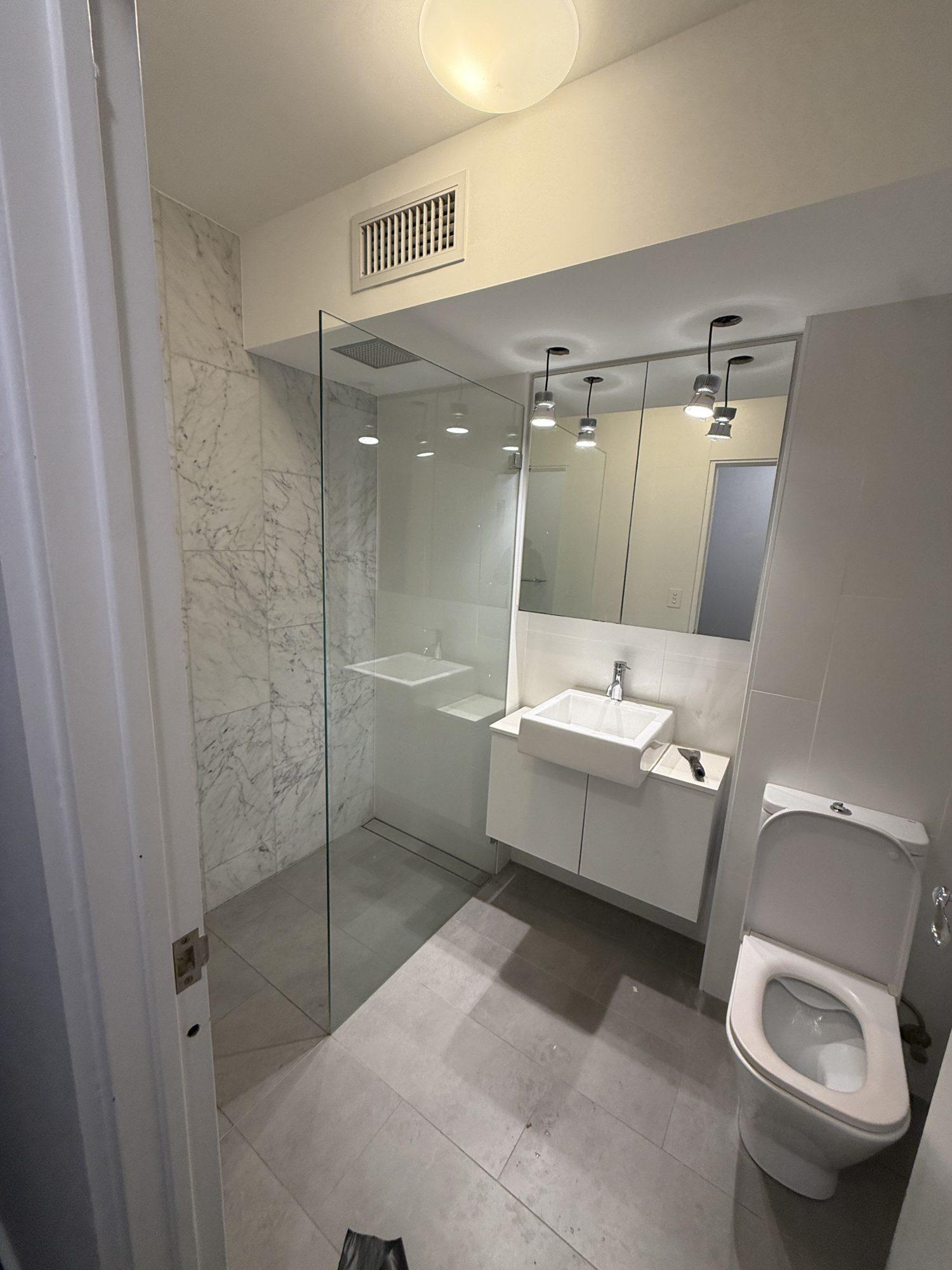 Clean apartment bathroom with marble shower and vanity after the ceiling panel removal