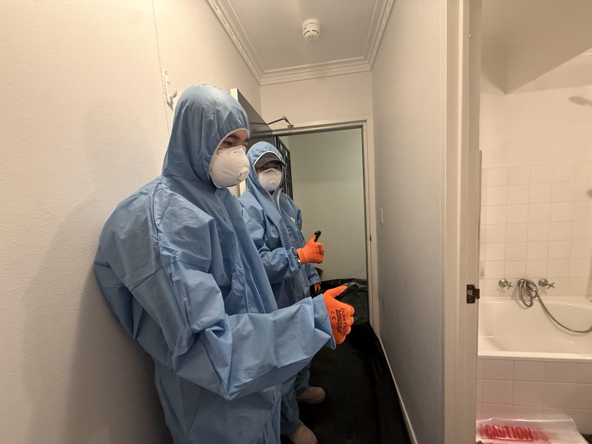 Two HazWreck removalists in disposable coveralls, P2 respirators and gloves in an apartment hallway