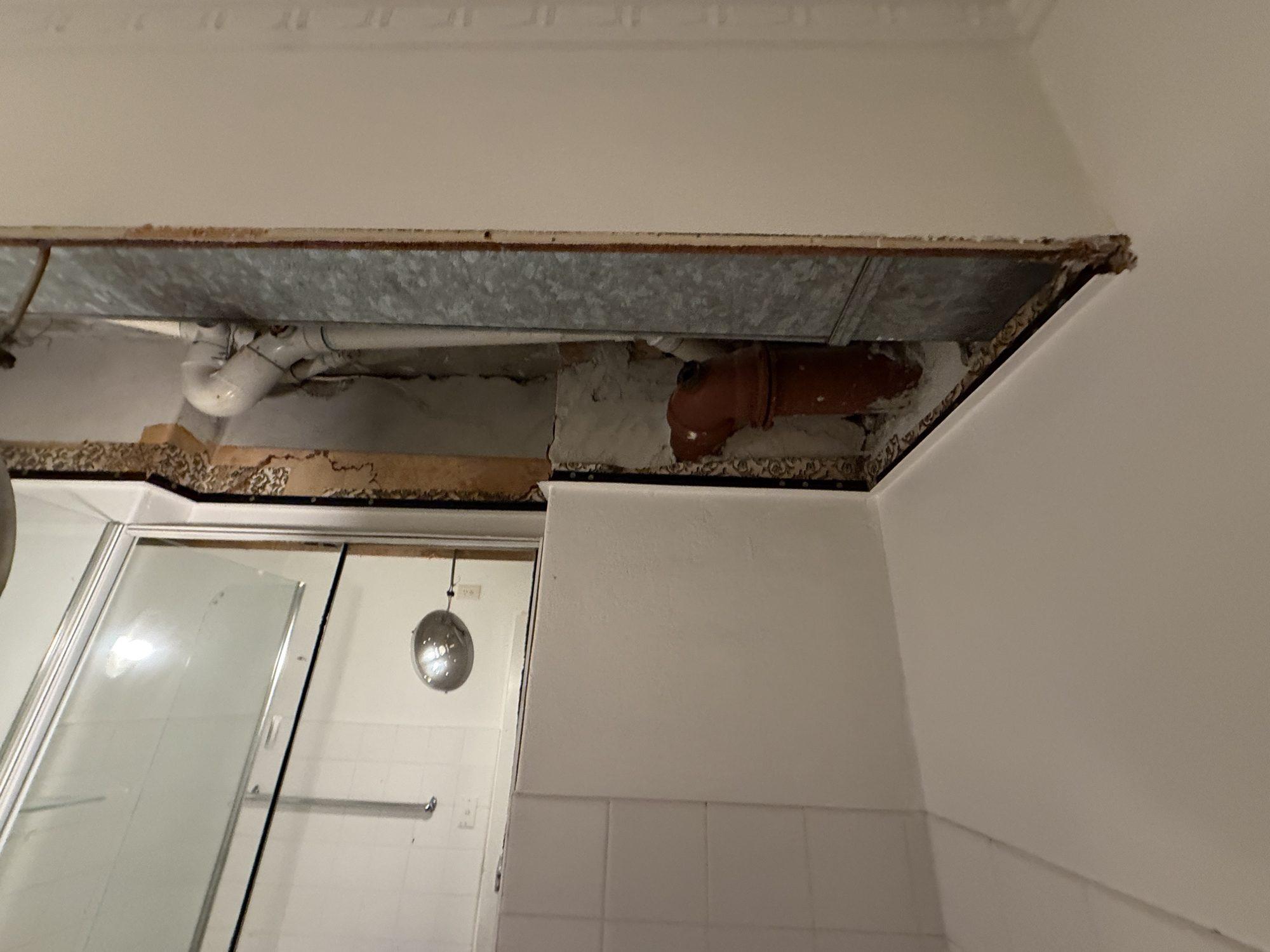 Ceiling cavity exposed above a shower after the asbestos panel was removed, showing the duct and pipework