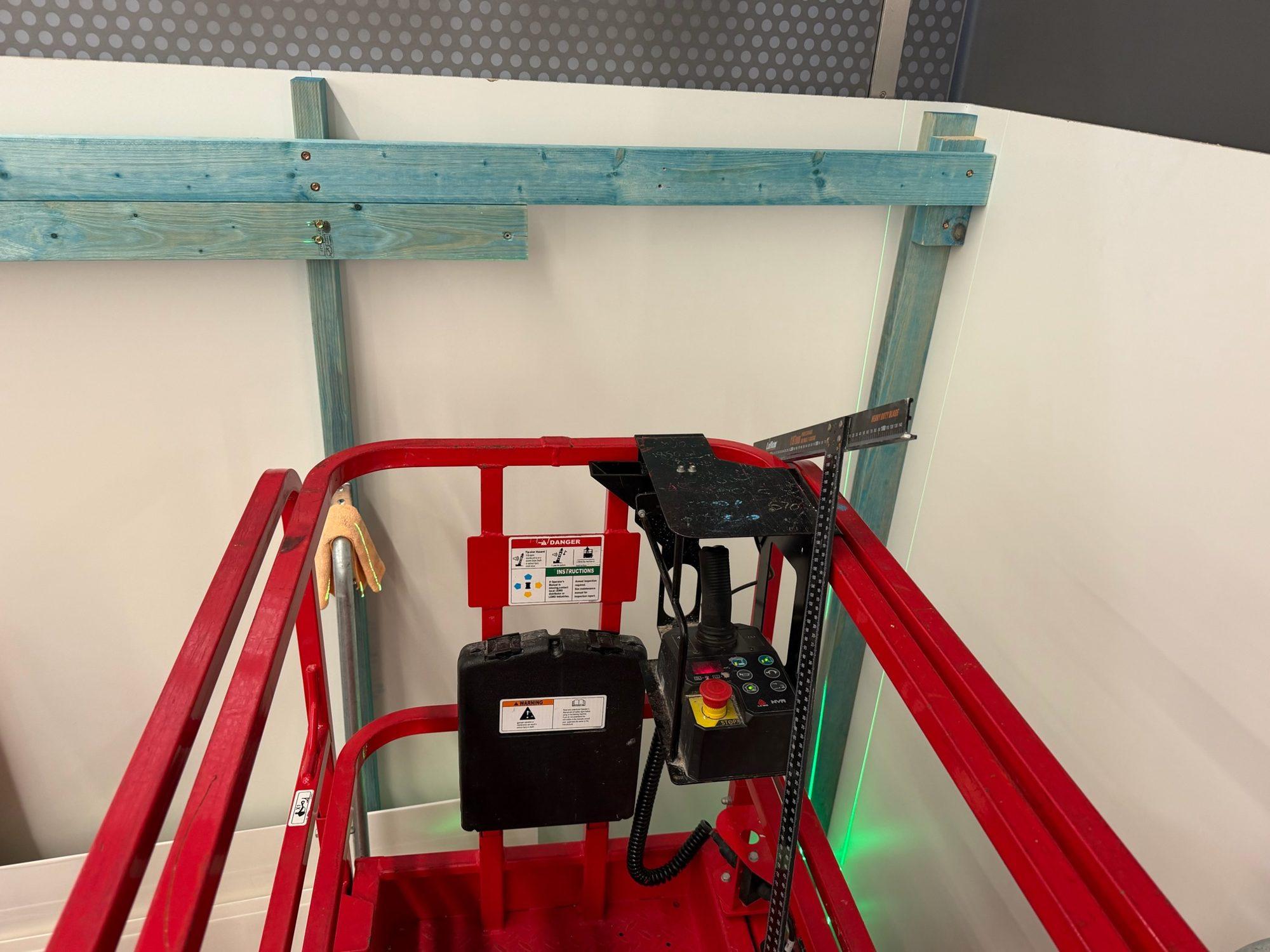 Red scissor lift basket beneath the arrivals hall ceiling at Sydney Airport T1, with a green laser line marking the opening