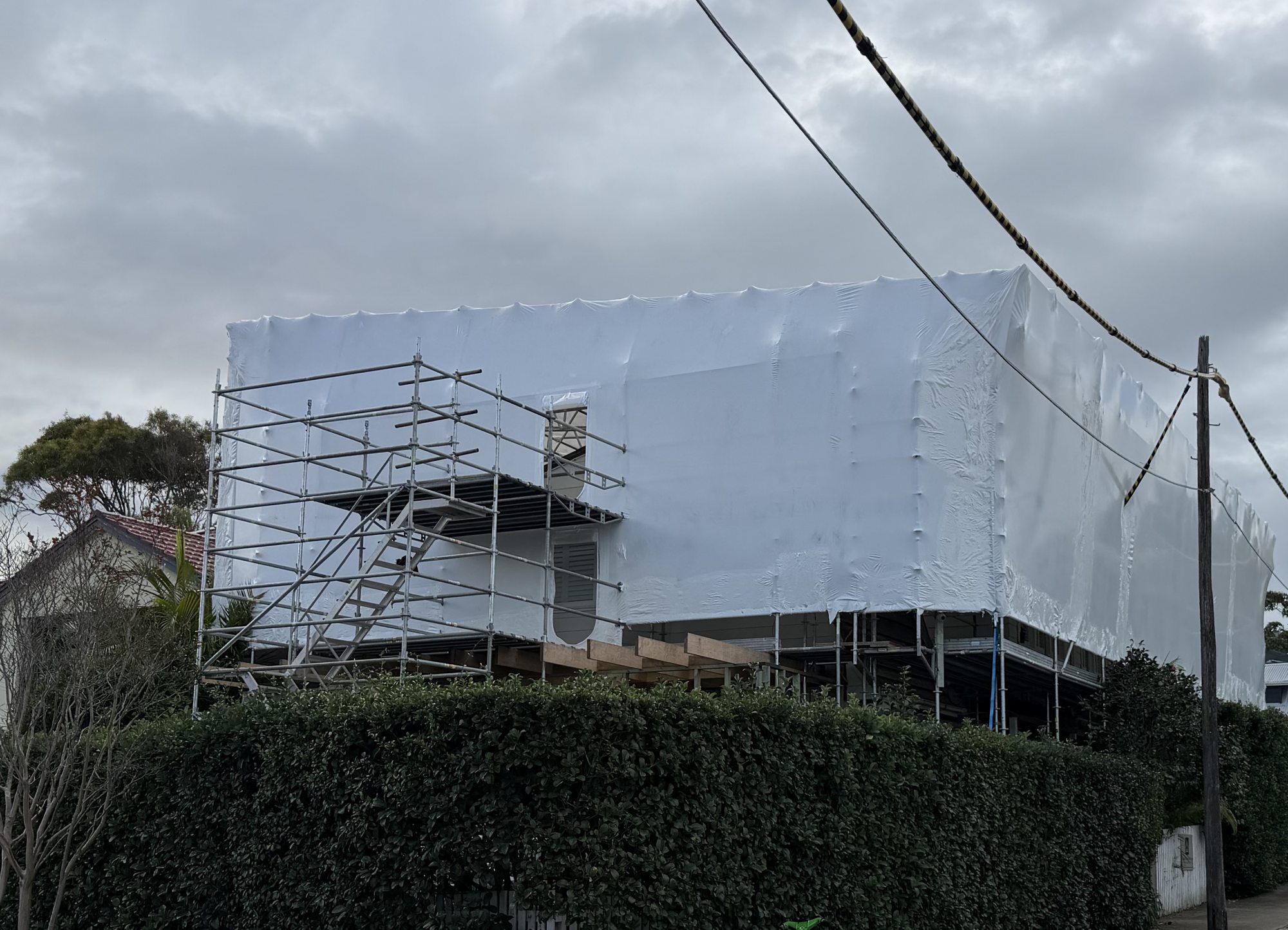A North Bondi house fully enclosed in white shrink-wrapped scaffold containment during renovation asbestos removal