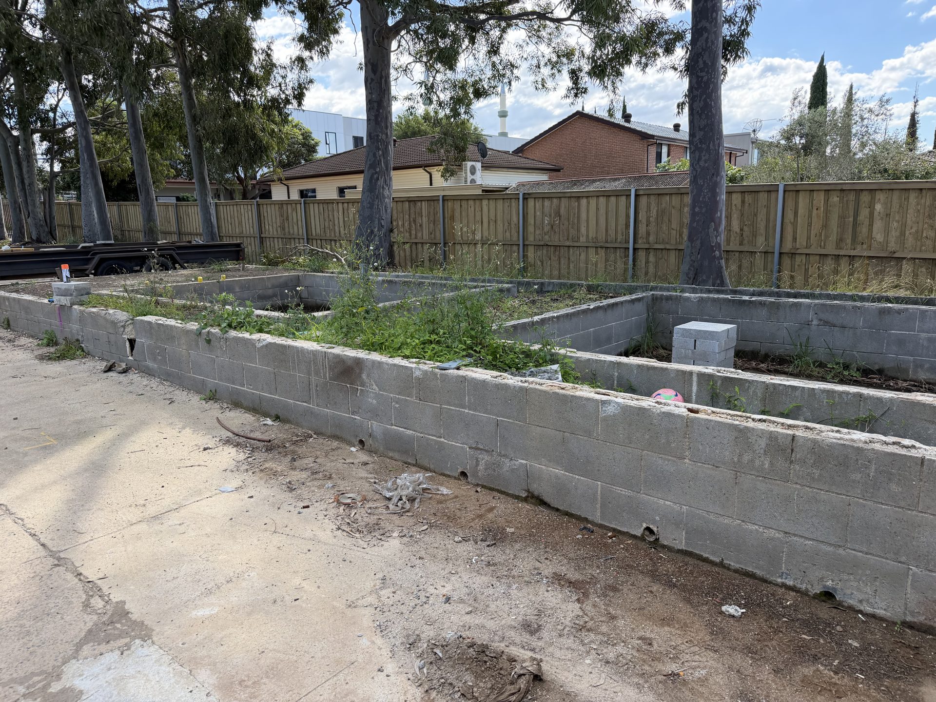 Long concrete block planter beds along the fence line at an Auburn school site before emergency demolition