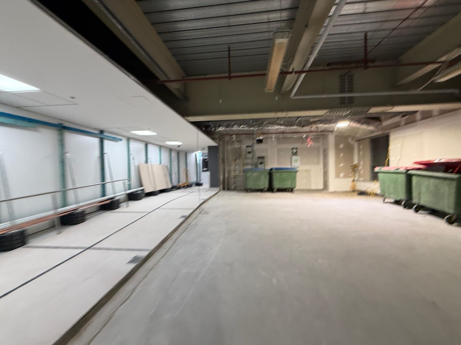 Back-of-house area inside Sydney Airport T1 cleared to bare slab at the end of an overnight shift, with bins staged for the waste route